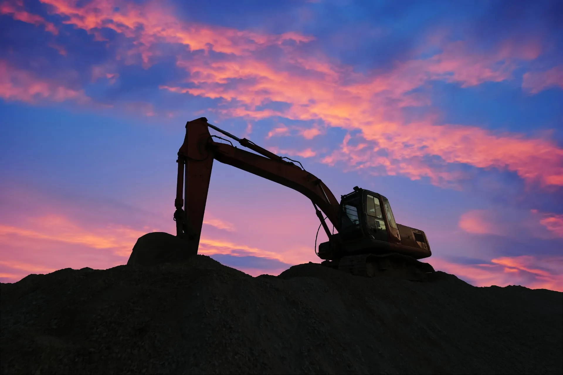 Excavation contractor excavator on a dirt stockpile at sunset in the Phoenix, AZ desert
