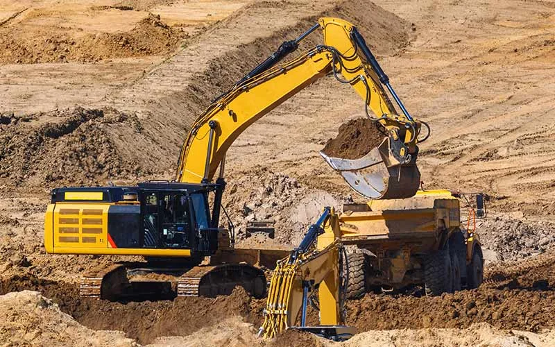 Tracked excavator loading spoil into an articulated dump truck on a Phoenician Excavation Company earthwork site